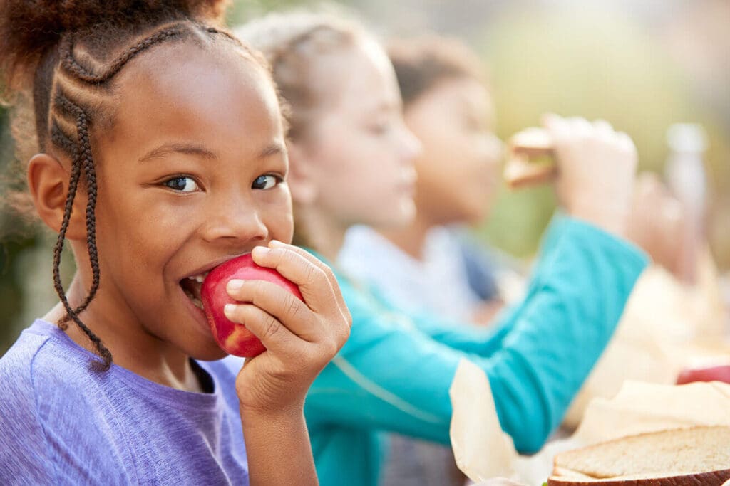 Children eating healthy lunches as an example of a nonprofit mission to address child hunger and food deserts. Nonprofit marketing budgets must generate enough support to further the mission.