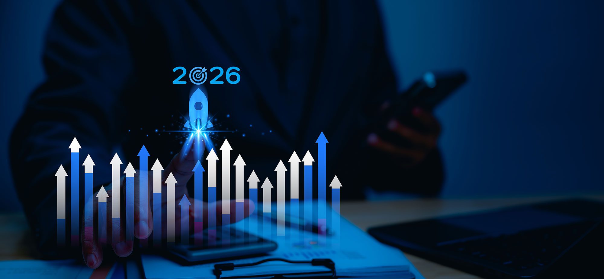 Image of person at desk holding phone with graphics overlaid showing "2026"