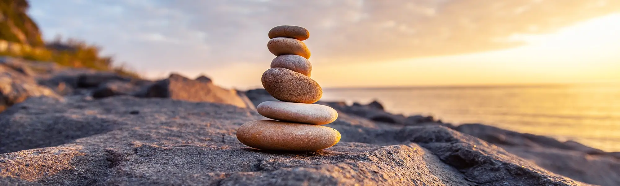 Stack of balanced rocks on a cliff over the ocean at sunset